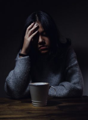 A depressed woman sits alone at a table holding her head